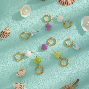Détail de boucles d'oreilles en forme de coquillages colorés sur un fond de thème marin turquoise