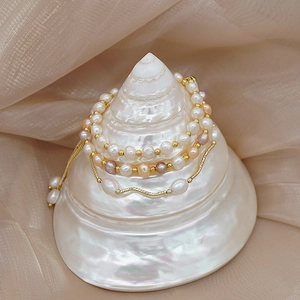 Detail of freshwater pearl bracelets with gold beads draped over a white seashell decor