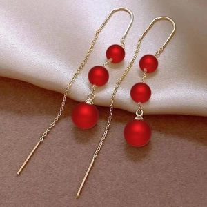 Detail of long gold chain earrings featuring three matte red beads and silk backdrop