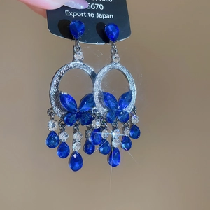 Detailed view of silver needle drop earrings with blue butterfly and long diamond tassels