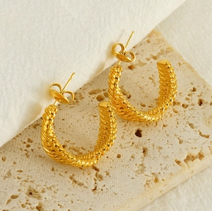 Detailed view of gold twisted texture C-shape earrings on a beige stone block