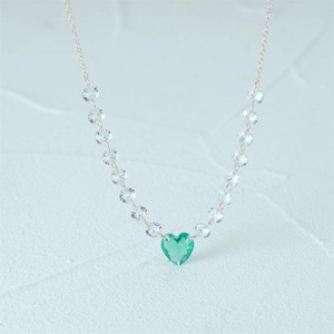 Macro shot of silver necklace with heart-shaped green gemstone and clear crystal link chain