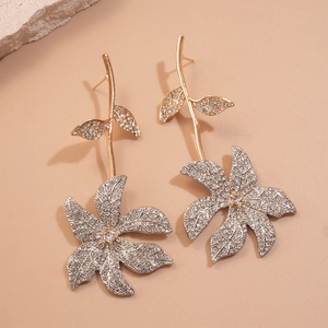 Macro detail of gold flower earrings with crystals on a textured stone surface