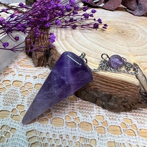 Detail of amethyst pendulum crystal with silver chain on wooden and lace background
