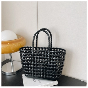 Detail of black woven hollow tote bag shown in a cozy home setting with warm lighting