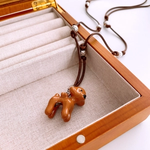 Détail macro du pendentif chiot marron sur cordon tressé posé sur une boîte en bois