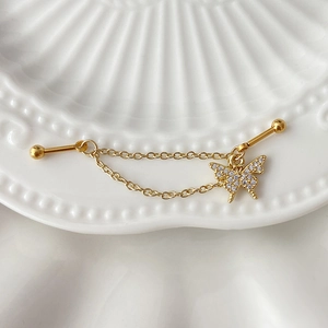 Detail of gold barbell earring with double chain and rhinestone butterfly pendant