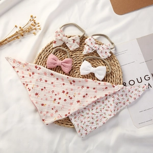Flat lay of baby cotton gauze bibs and floral bow headbands set on a rustic mat