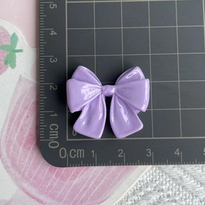 Top-down view of a purple resin bow accessory measuring 2.5cm by 3.5cm on a ruler