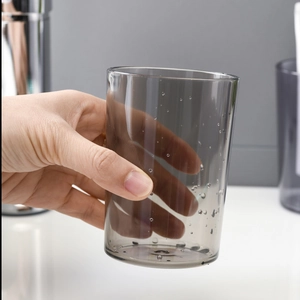 Gobelet de rinçage minimaliste en plastique gris fumé tenu dans une salle de bain moderne