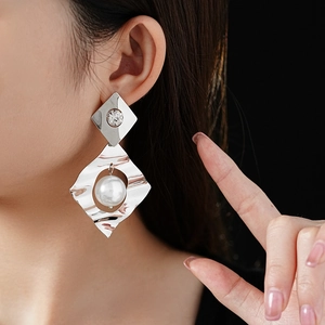 Detailed view of silver geometric earrings with pearls and crystals on female model