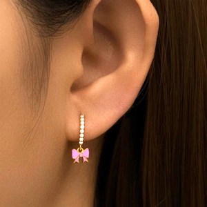 Pink enamel bow earrings with gold plating and sparkling white crystals on model