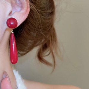 Close-up of a red teardrop pendant earring worn on ear with polished finish