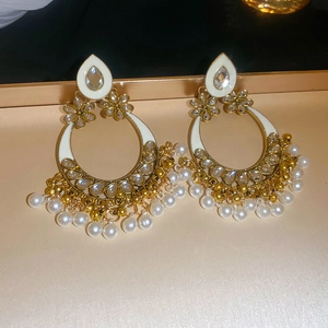 Detail of ethnic gold earrings with white enamel, rhinestones and pearl tassels