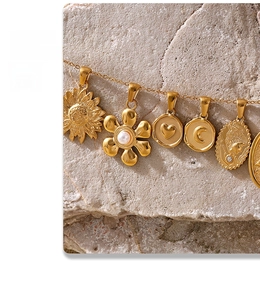 Detail of 18K gold-plated necklace with floral and heart pendants on textured stone