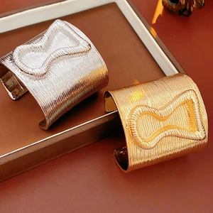Close-up of gold and silver linear texture cuff bracelets on a brown leather tray