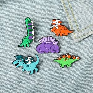 Set of five cartoon dinosaur enamel pins with books on blue denim background