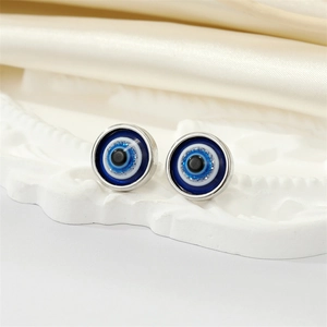 Close-up of resin Evil Eye stud earrings on a white embossed tray and silk fabric