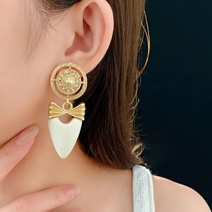 Close-up of vintage bow heart earring with gold plating and white stone on model