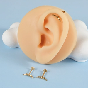 Detailed view of three gold stainless steel curved labret studs on a silicone ear model