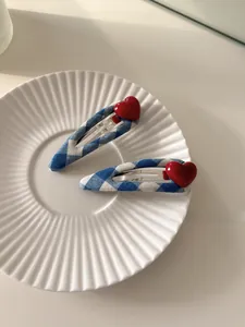 Close-up of blue and white checkered hair clips with red 3D hearts in a ceramic dish