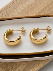 Vue macro des boucles d'oreilles dorées en forme de C sur un plateau en céramique