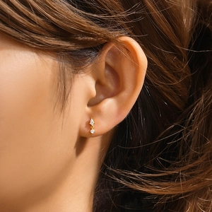 Close-up of a gold geometric rhombus stud earring with a diamond accent on a model's ear