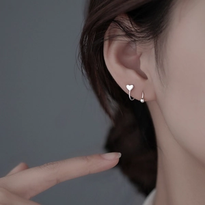 Detail of silver heart and bead screw back earrings worn on a model's ear cartilage