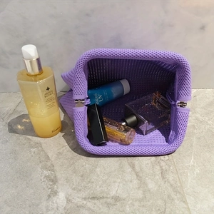 Lavender striped knitted makeup bag with metal frame showing sunscreen and perfume