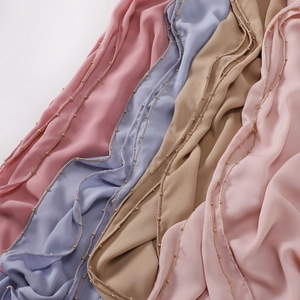 Detail of silk scarves in pastel tones featuring delicate gold bead chain trimming