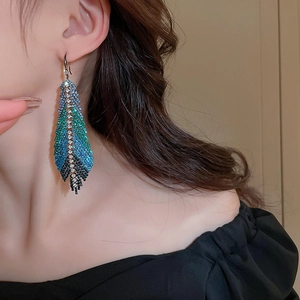 Macro view of crystal-encrusted feather earrings with blue and green gradient finish