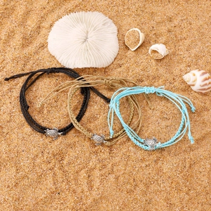 Detailed view of three handmade woven turtle anklets on a sandy beach background