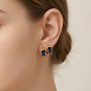 Close-up of golden stainless steel hoop earrings with rectangular blue sapphire stone