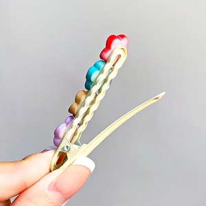 Handheld view of a colorful floral hair clip with red and purple resin flower charms