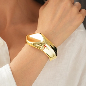 Macro view of wide irregular wave opening cuff bracelet in polished gold finish