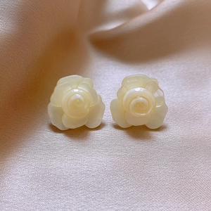 Macro detail of ivory resin flower stud earrings on soft beige silk fabric background