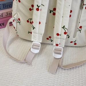 Detail of adjustable white strap buckle and red cherry print on corduroy backpack