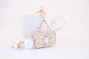 Detail of golden keychain with colorful rhinestone mini bag and white floral charm
