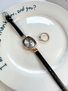 Close-up of vintage oval quartz watch with black leather strap and gold case in a dish