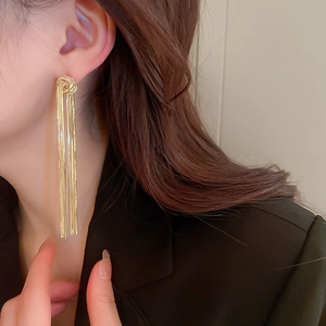 Close-up of elegant gold tassel earrings with intricate knot detail worn by a model