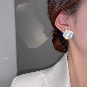 Close-up of elegant square cat eye stone earrings with zircon halo on model's ear