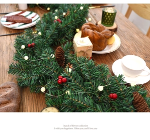 Close-up of 2.7m Christmas garland with pine cones, red berries and LED lights on wooden table