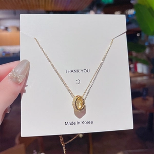 Close-up of golden triple-ring pendant necklace with micro-pave crystals on white card