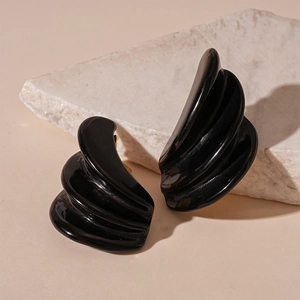 Detail of black resin triple-layer wavy earrings on a textured stone over light background