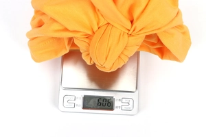 Detail view of the orange cotton turban beanie showing its 60.6g weight on a digital scale
