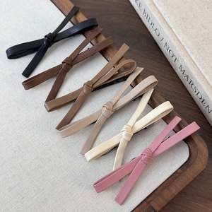 Detailed set of six faux leather bow hair clips in various earthy tones on a linen mat