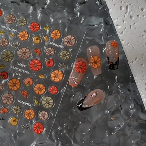 Detail of 3D Halloween pumpkin and maple leaf nail stickers on manicured nails