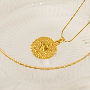 Macro detail of Scorpio zodiac pendant in 18k gold finish on a glass tray