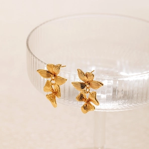 Irregular vintage gold floral earrings with layered leaf design on a glass rim