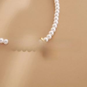 Detail of white pearl necklace with a gold circular Good Luck charm pendant